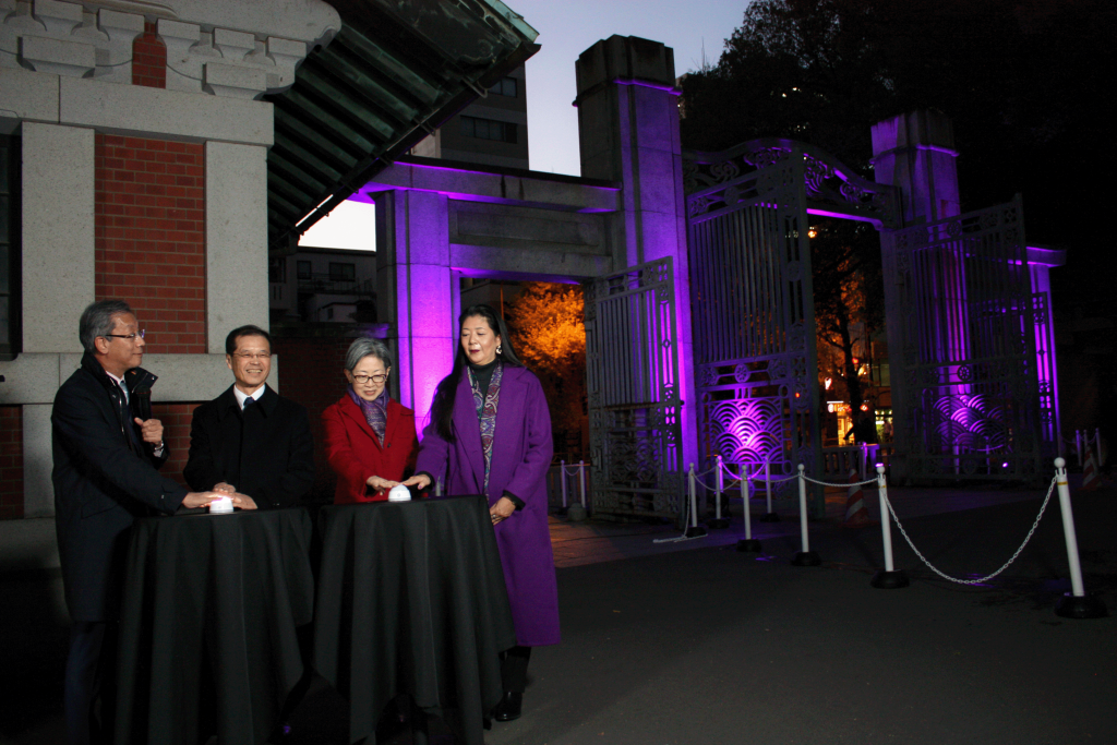点灯式の様子。
藤井輝夫総長、相原博昭理事・副学長、林香里理事・副学長、石井リーサ明理さんが横並びになってボタンを押し、正門が紫色に照らされた。